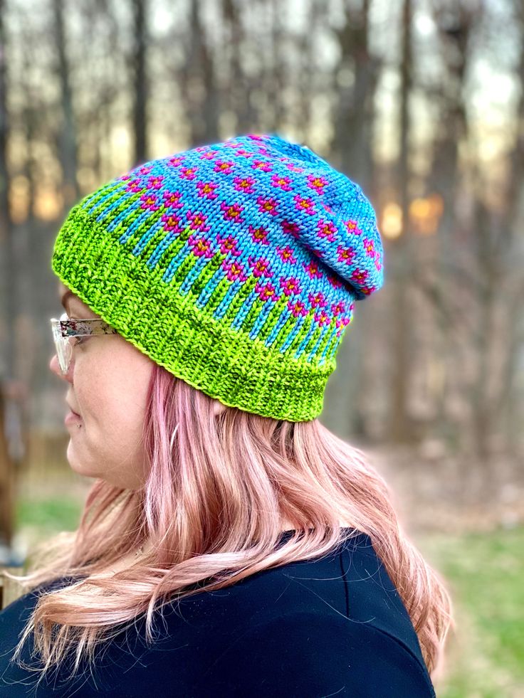 a woman with pink hair wearing a green and blue knitted hat in the woods