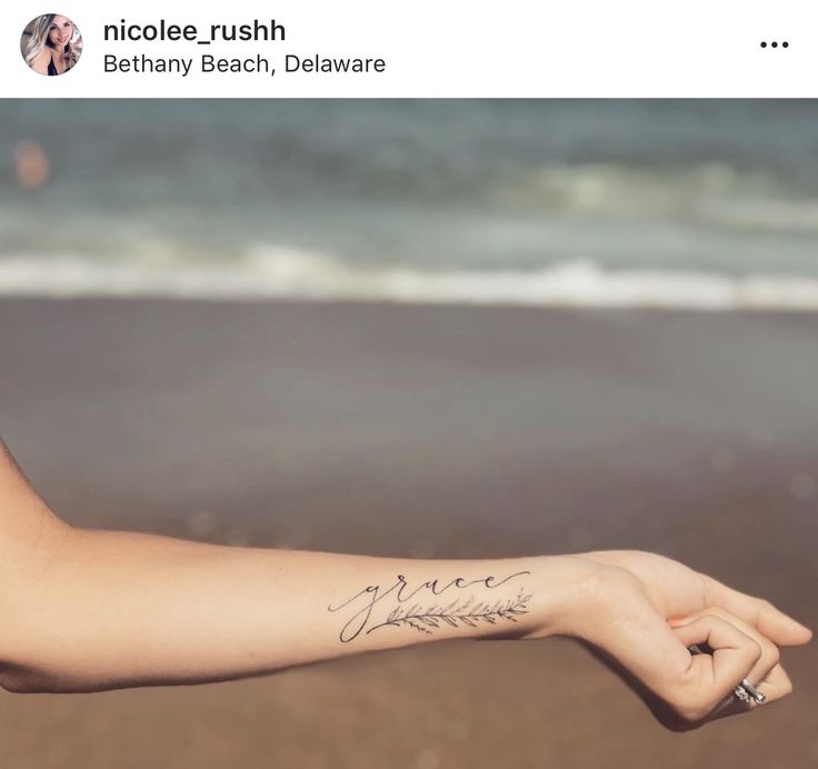 a woman's arm with a tattoo on it and the ocean in the background