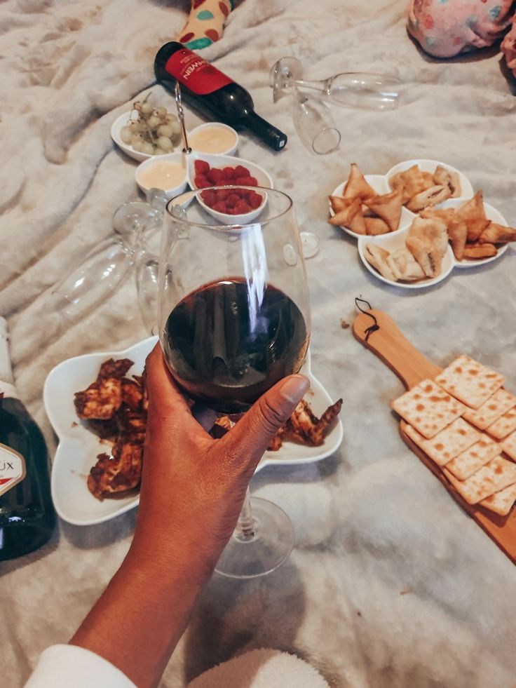 a person holding a glass of wine in front of some food on plates and bottles