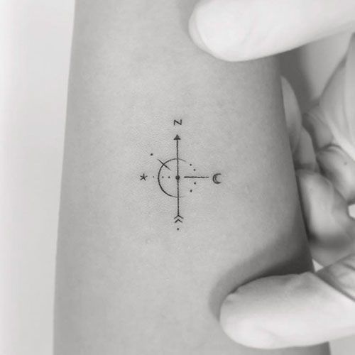 a woman's arm with a small compass tattoo on it