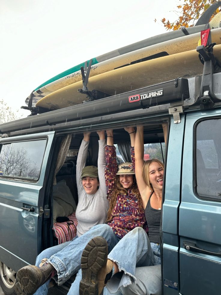 three people sitting in the back of a van with surfboards on their heads and feet