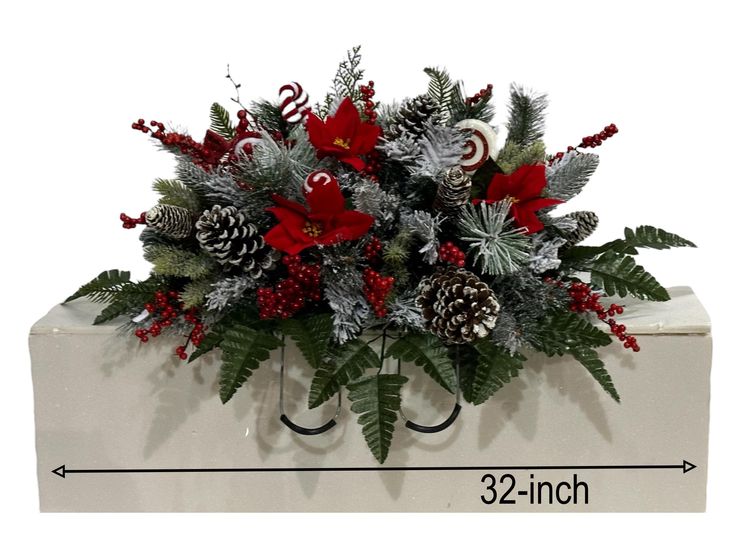 a christmas arrangement with pine cones, holly and candy canes in a white box