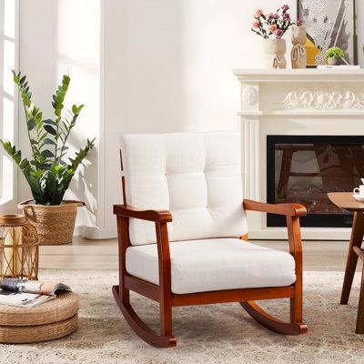 a white rocking chair sitting in front of a fire place next to a wooden table