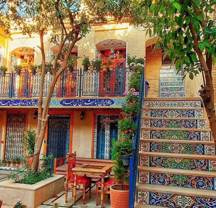 an outdoor patio area with stairs, tables and potted plants in front of colorfully painted balconies