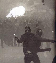 a man wearing a gas mask and holding a cell phone in front of a crowd