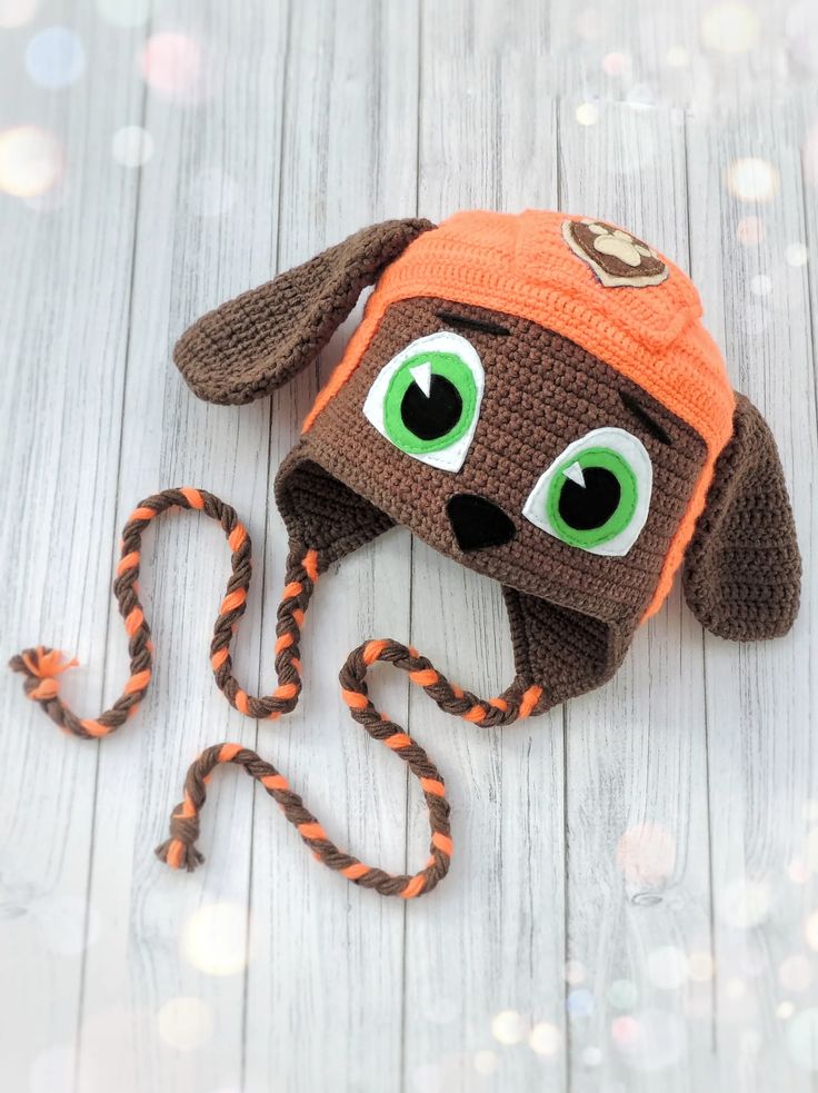 a crocheted brown dog hat with green eyes and orange earflaps