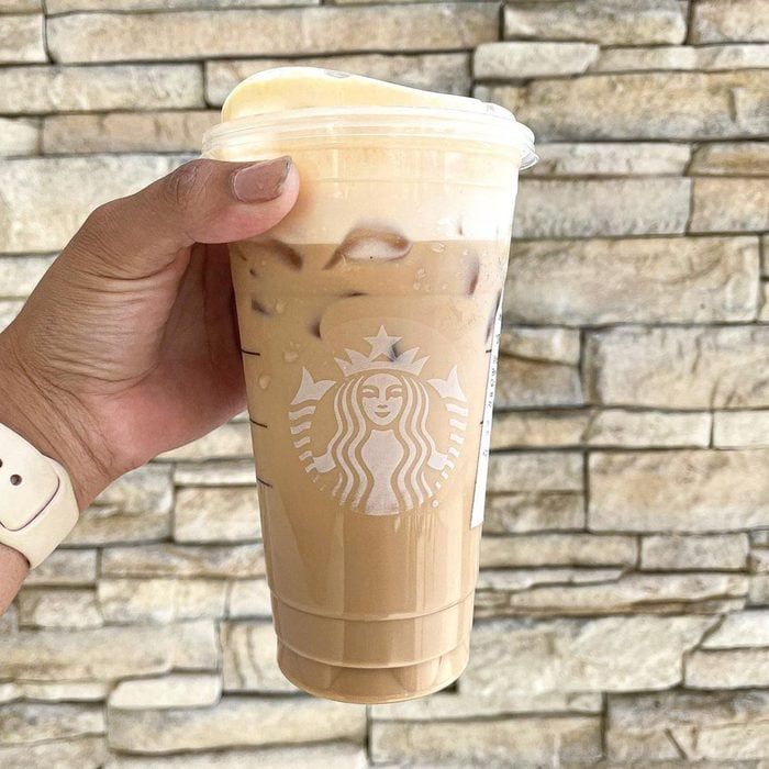 a hand holding up a starbucks drink in front of a brick wall