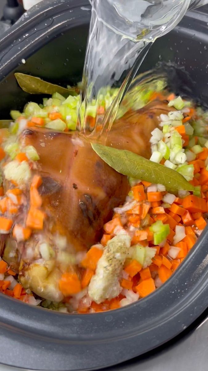 someone is pouring water into a slow cooker filled with carrots, celery and onions