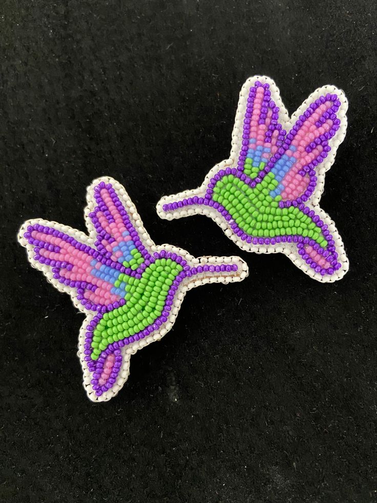 two purple and green beaded hummingbirds on a black surface