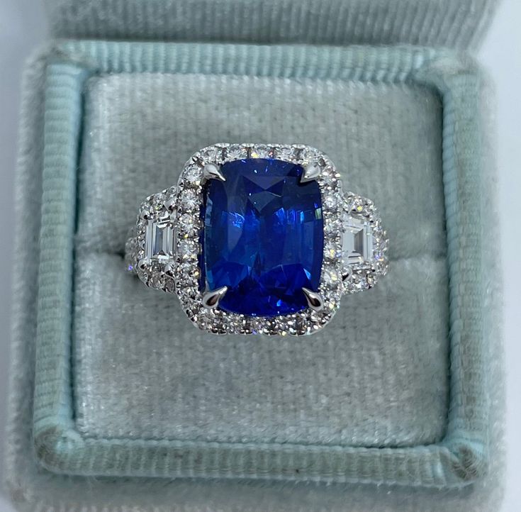 an engagement ring with a blue stone surrounded by white and clear cubicles in a velvet box