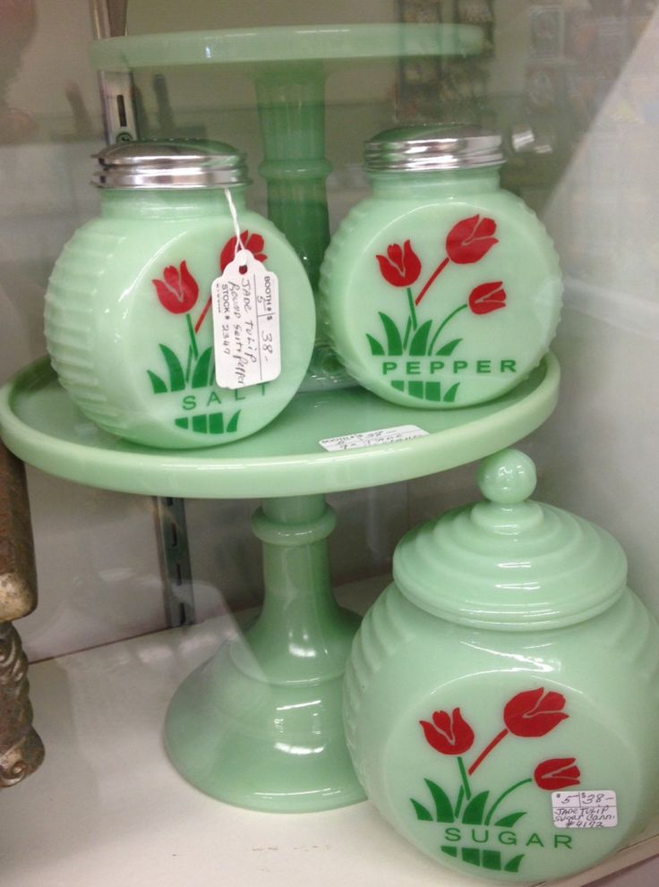 three green vases with red flowers on them sitting on a shelf in a glass case