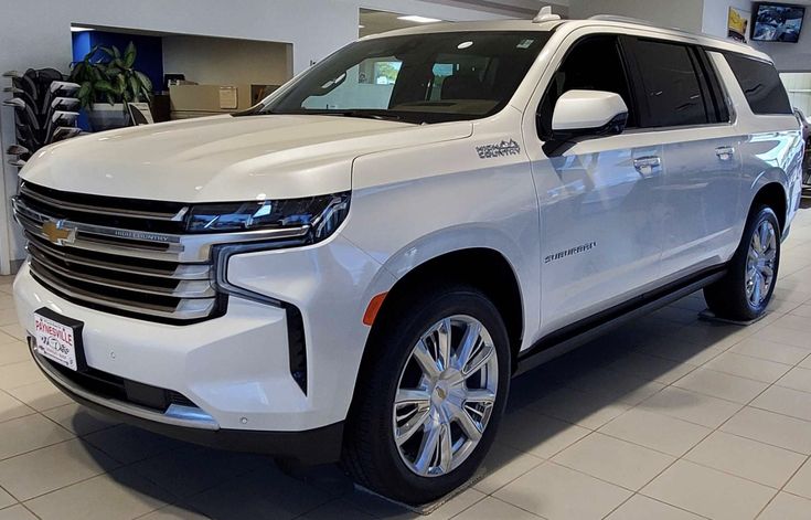 a white chevrolet suv is parked in a showroom with other cars on the floor