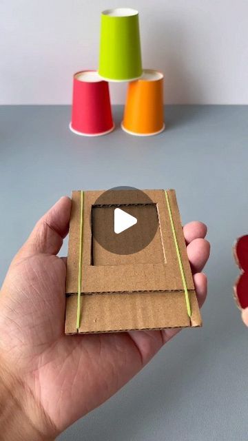 a hand holding a piece of cardboard with a video playing on it and some spools of thread in the background