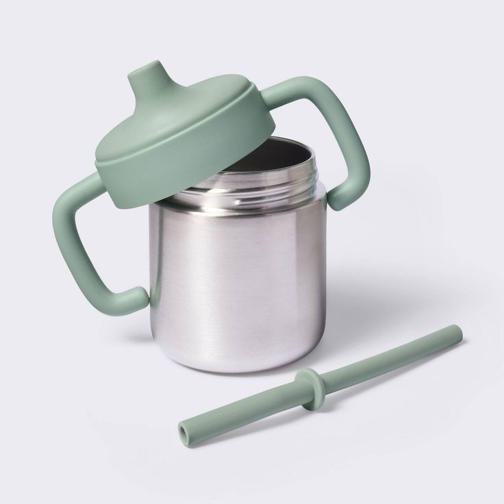 a cup with a lid and handle next to a metal container on a white background