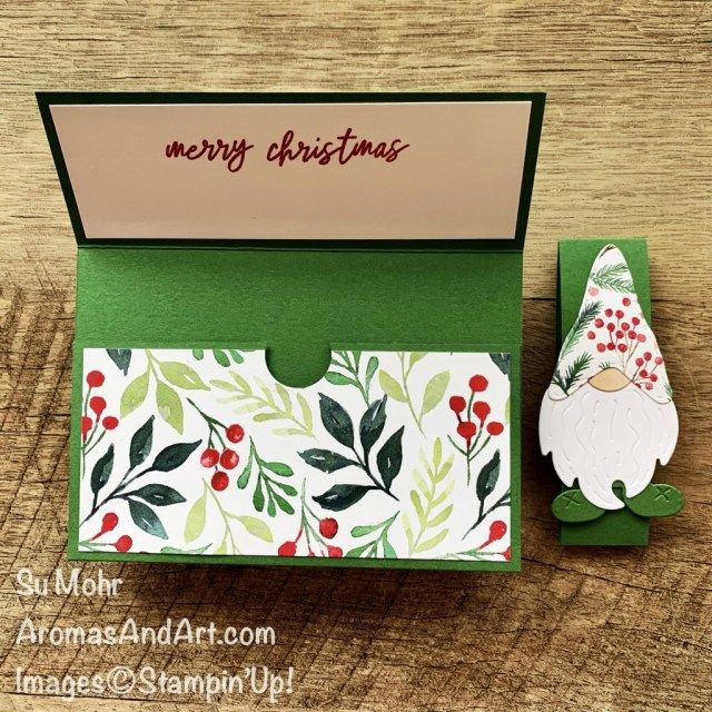 an open christmas card with a gnome and holly leaves on it, sitting next to a green box