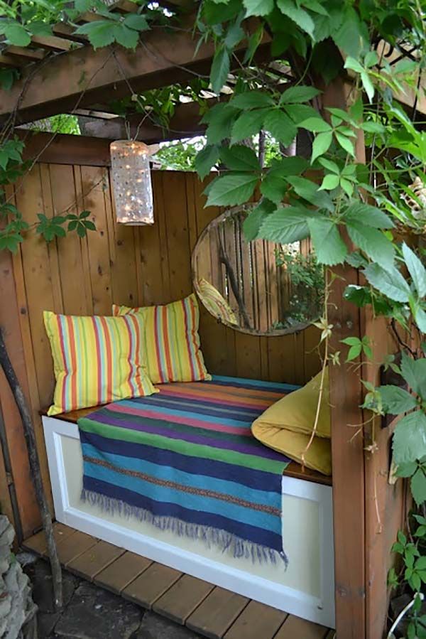 a bed sitting under a tree next to a wooden fence with green leaves on it