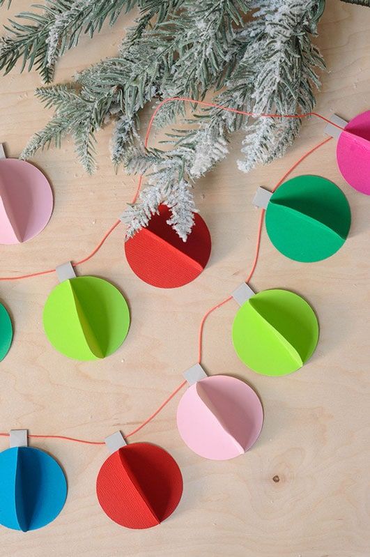 some paper ornaments are hanging from a tree branch and on the table is a christmas ornament