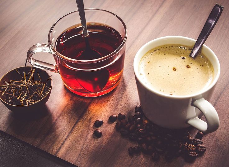 a cup of coffee next to a mug of tea and beans on a wooden table