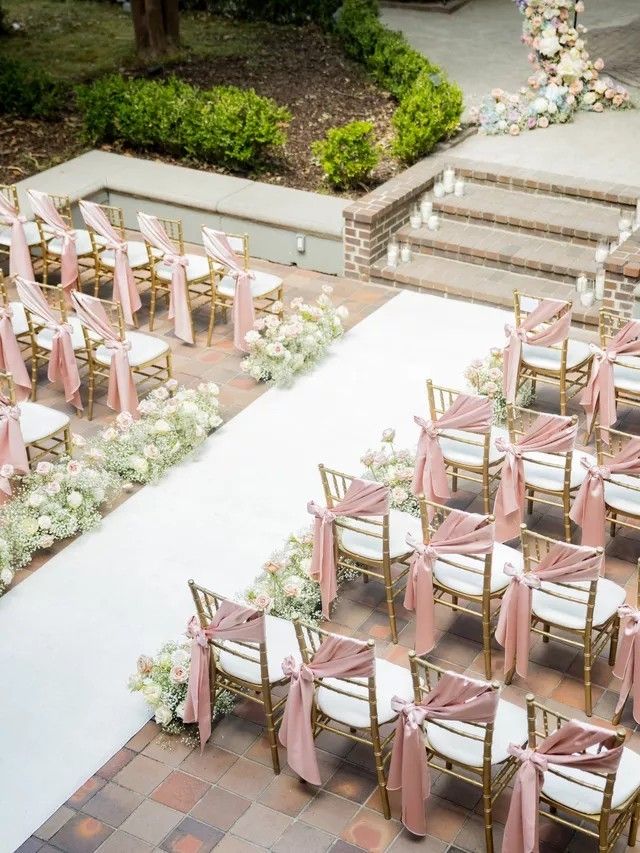 rows of chairs with pink sashes and white flowers on them are set up for an outdoor ceremony