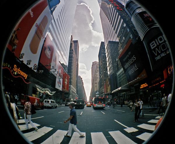 a man walking across a cross walk in the middle of a city with tall buildings