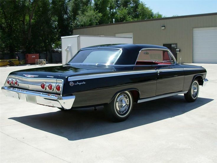 an old black car parked in front of a garage