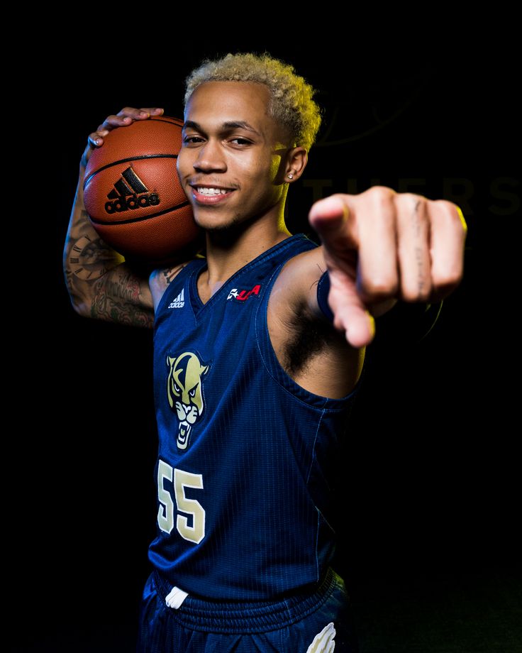 a man holding a basketball in his right hand and pointing at the camera with both hands