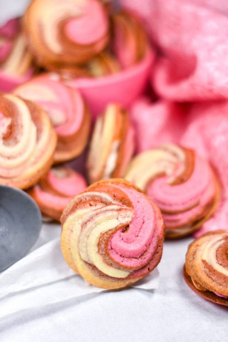 some pink and yellow pastries are on a white table cloth next to bowls of other pastries