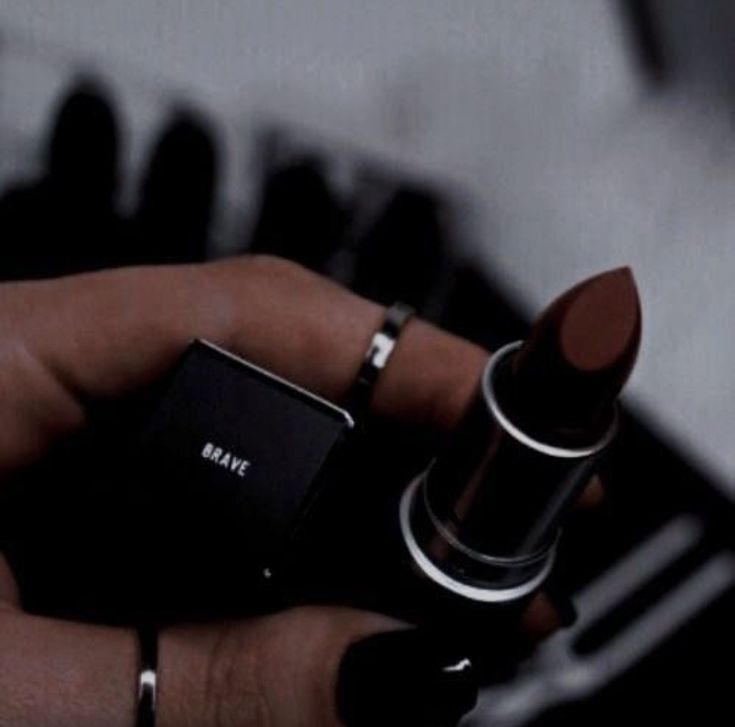 a person holding a lipstick in their left hand and an electronic device in the background