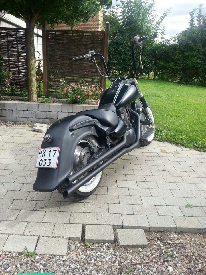 a black motorcycle parked on top of a brick road next to a green lawn and fence