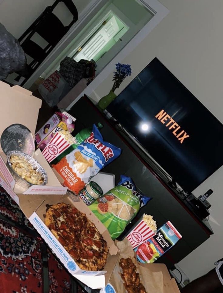 two pizzas and snacks are sitting on the floor in front of a television