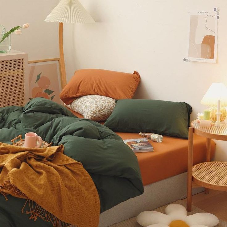 an unmade bed with green and orange comforter on it in a white room