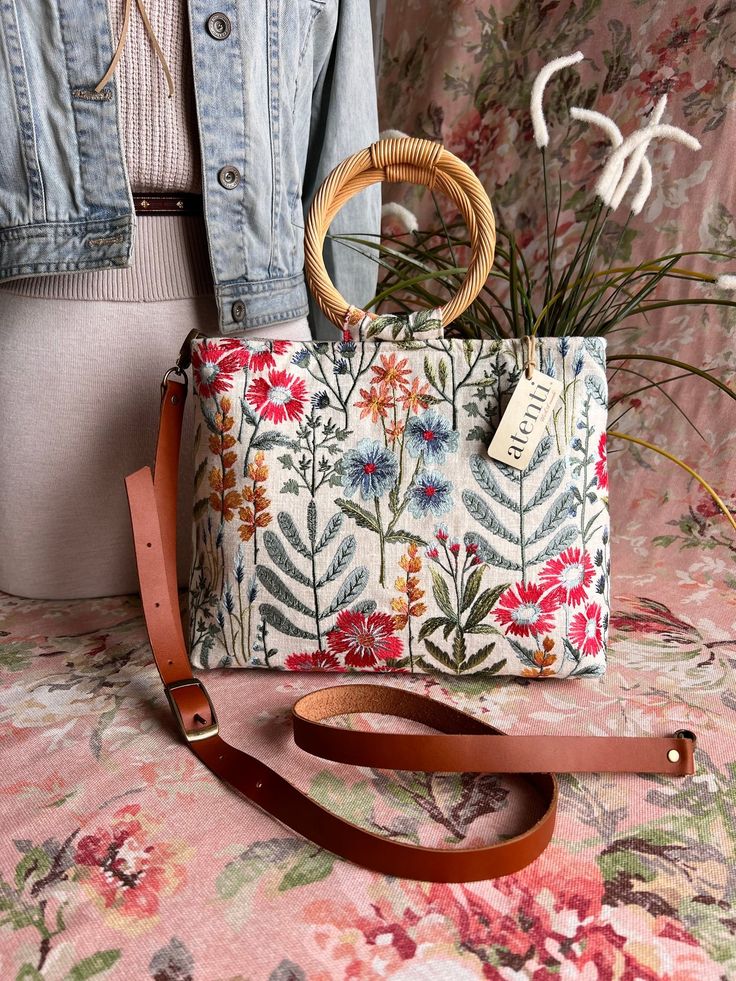 The Atenti Wildflower Tall Fifi is adorned with beautifully embroidered spring flowers on a heavy duck canvas and is sure to become a new, fresh favorite. Stow away all your essentials and hit the town!  Crafted with the utmost care and attention to detail, this bag is sure to make a statement wherever you go. The Tall Fifi has a chic silhouette - compact but roomy with round straw handles and a cream denim interior.

Atenti's Tall Fifi Wildflower Handbag is a taller version of Atenti Fifi. Your Spring Flower Shoulder Bag With Adjustable Strap, Flower Shaped Shoulder Bag With Adjustable Strap For Spring, Spring Beige Bag With Floral Embroidery, Spring Rectangular Shoulder Bag With Floral Embroidery, Spring Beige Floral Embroidered Bag, Spring Floral Embroidered Shoulder Bag, Spring Floral Embroidery Shoulder Bag, Spring Beige Shoulder Bag With Floral Embroidery, Spring Travel Shoulder Bag With Embroidery