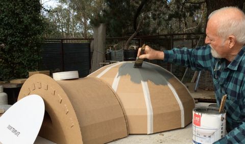 an older man is painting the outside of a large cardboard structure with paint on it