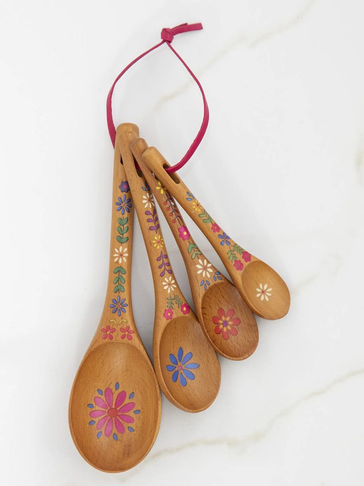 four wooden spoons with designs on them hanging from a red string against a white background