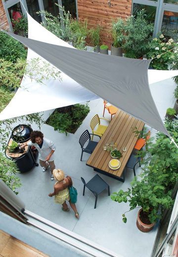 an overhead view of some people sitting at a table under a white awning in a garden