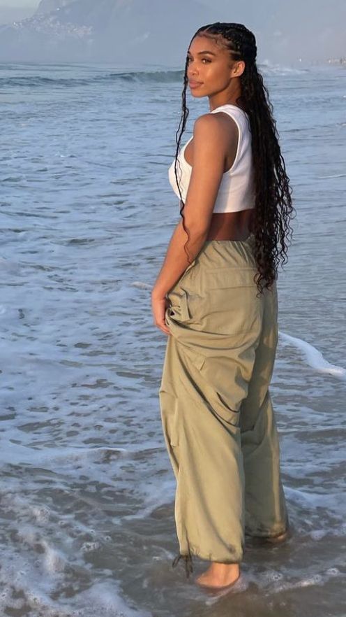 a woman is standing in the water at the beach with her long hair pulled back