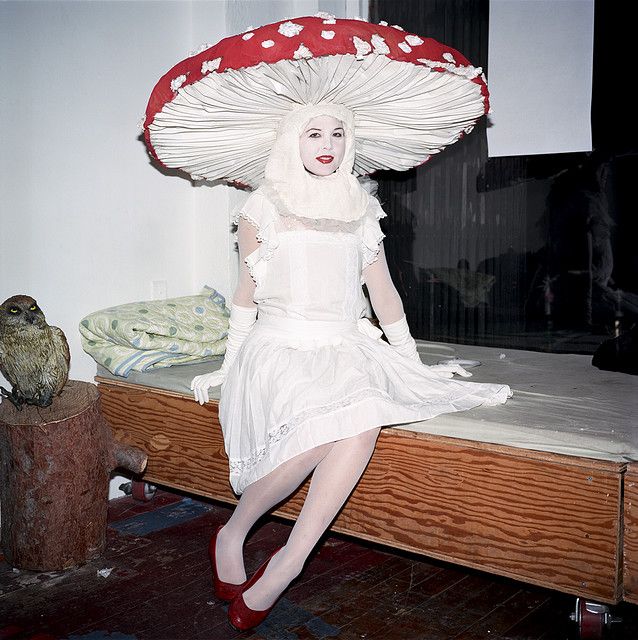 a woman in white dress sitting on top of a bed with an umbrella over her head