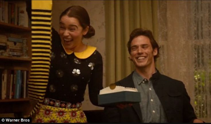 a man and woman holding a cake in front of a book shelf with books on it