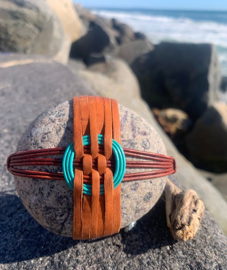 a piece of jewelry sitting on top of a rock next to the ocean and rocks