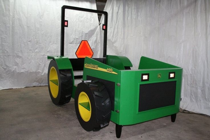 a green tractor with yellow wheels parked in front of a white wall and orange traffic sign