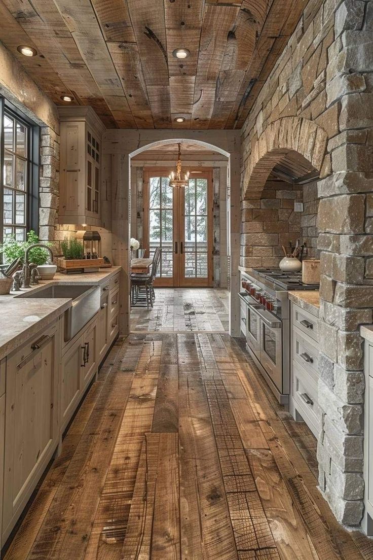 a large kitchen with wood floors and stone walls, along with an arched doorway leading to the dining room