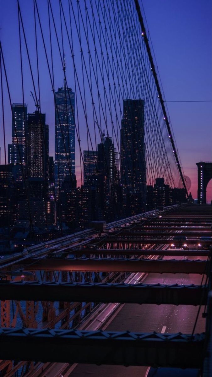 the city skyline is lit up at night as seen from across the brooklyn bridge in new york