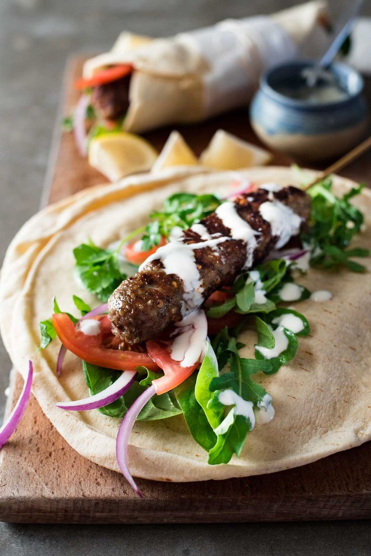 a pita filled with meat and veggies on top of a wooden cutting board