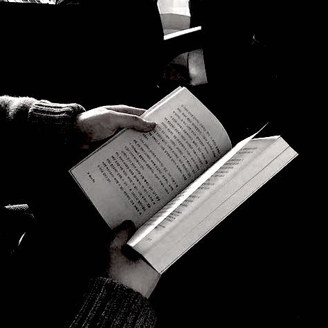 a person sitting down reading a book with their hands on top of the open book