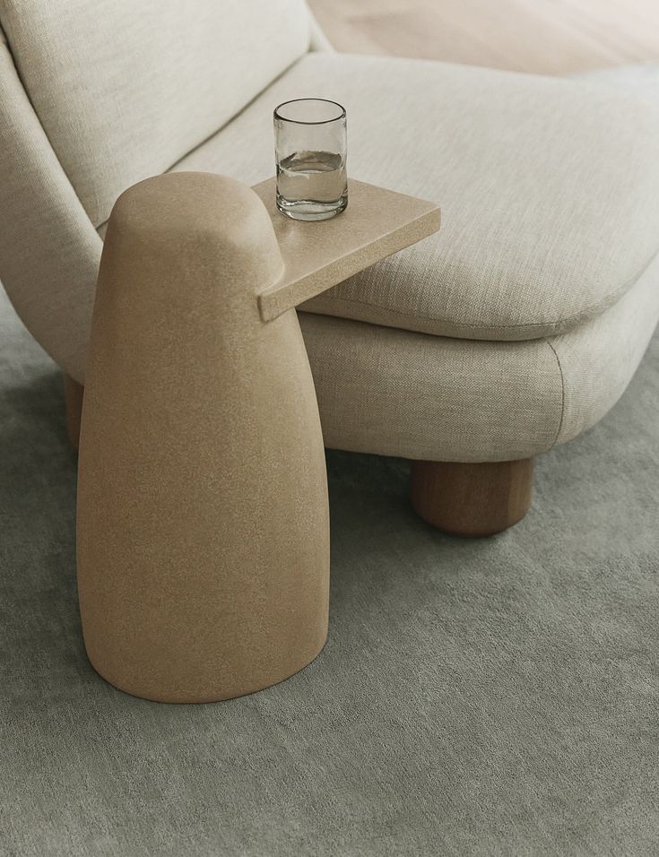 a small glass sitting on top of a table next to a chair and footstool