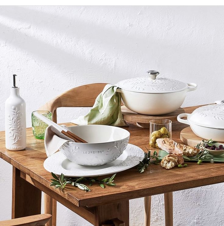 a wooden table topped with white bowls and plates