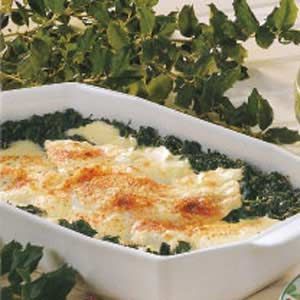 a casserole dish with spinach and cheese in it next to a glass of water