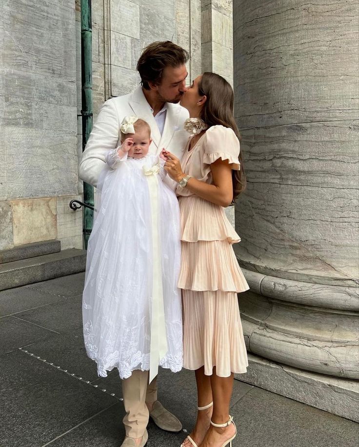 a man in a suit and tie kissing a woman wearing a white wedding dress while holding a baby