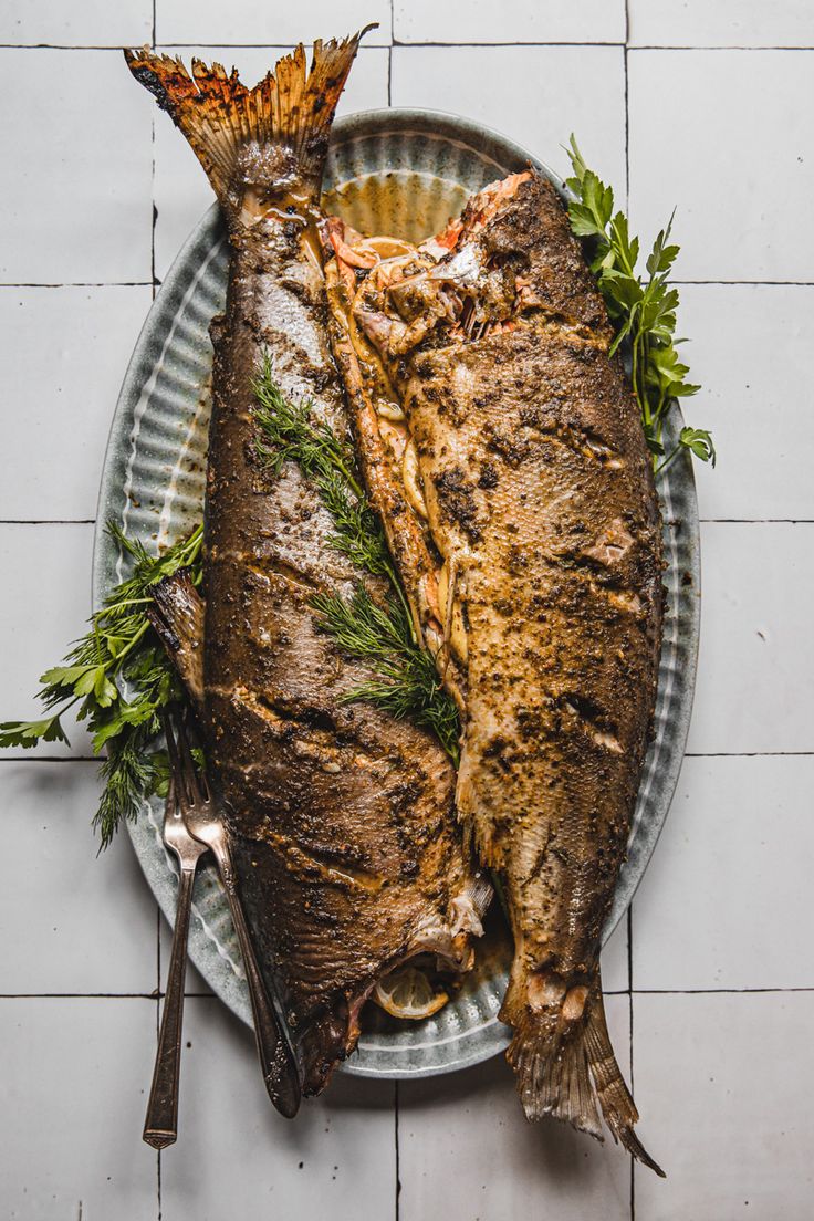 two large fish on a plate with herbs