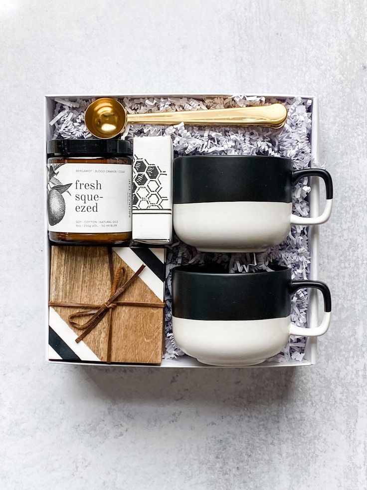 two coffee mugs in a gift box with spoon and crackers on the side